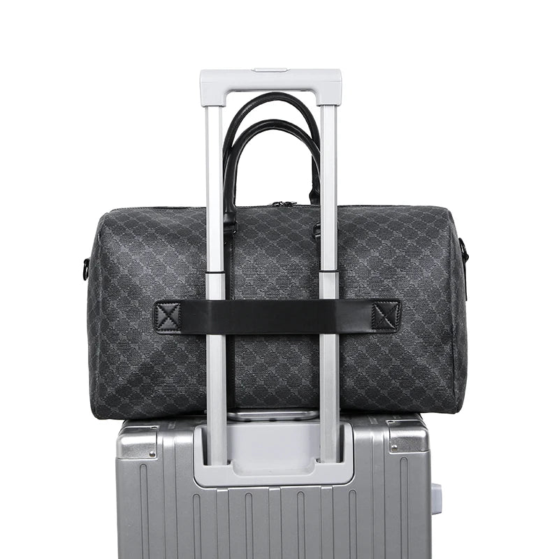 Gray checkered duffel bag with black strap on top of a silver suitcase.