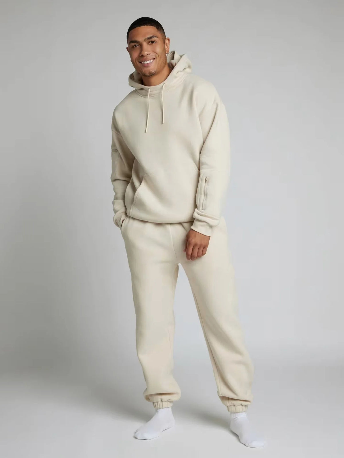Man wearing a beige hoodie and pants set on a plain background
