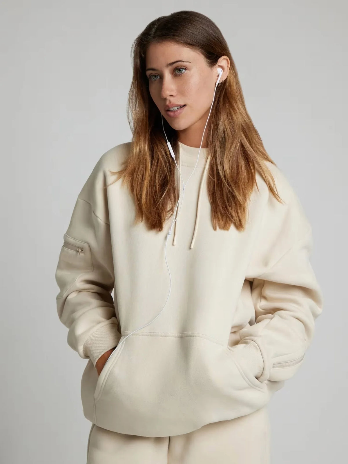 Woman wearing a beige hoodie with earphones on a plain background