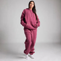 Person wearing a pink hoodie and pants set on a plain background