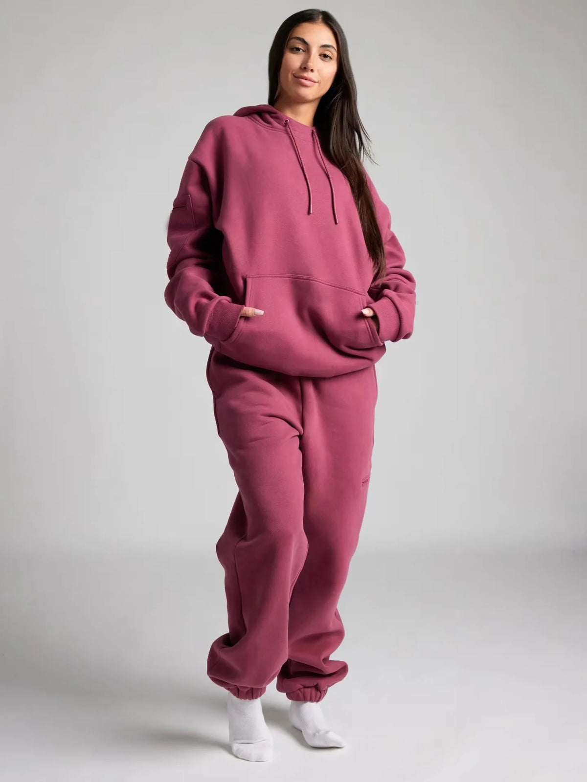 Person wearing a pink hoodie and pants set on a gray background