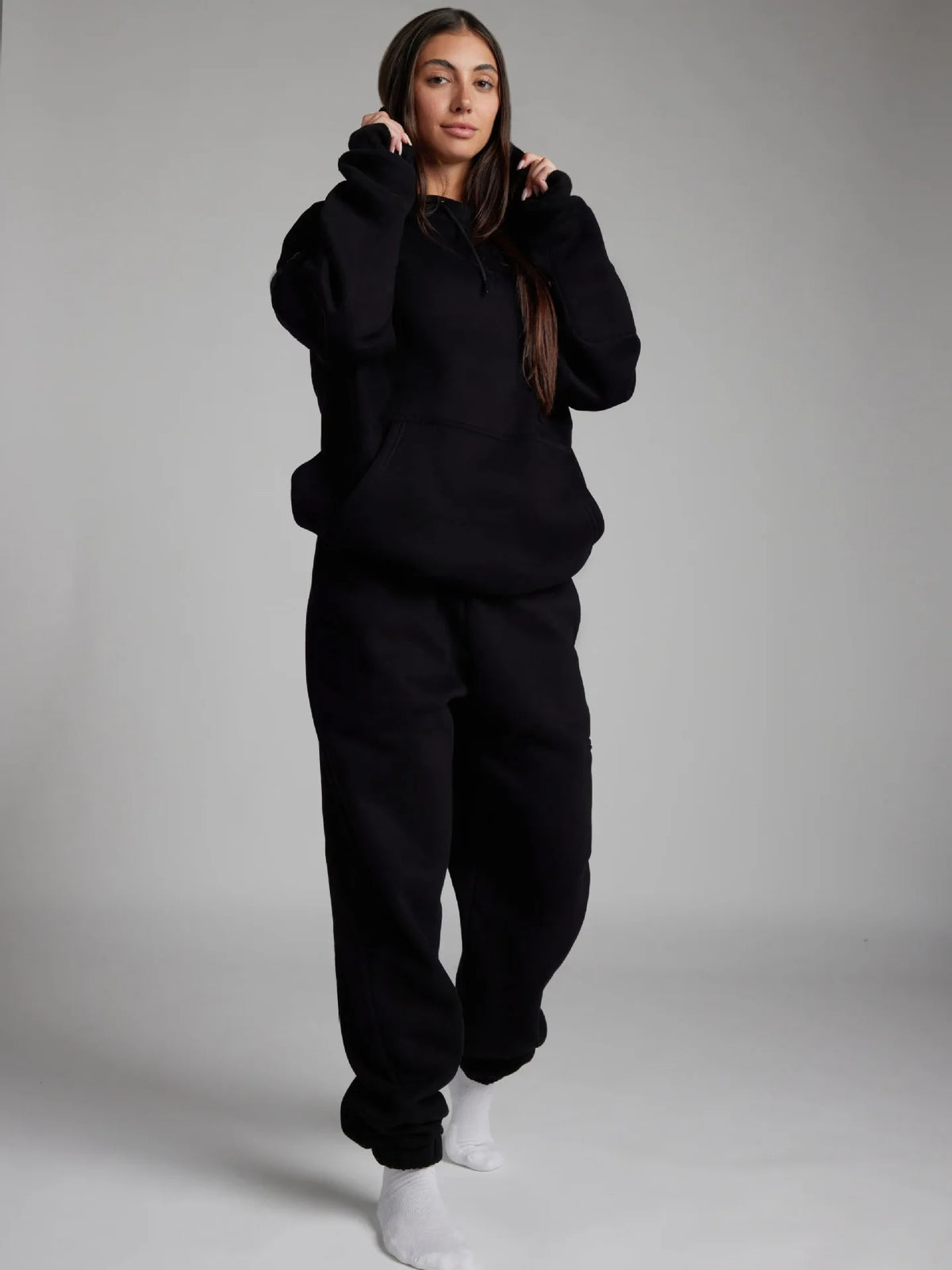 Person wearing a black hoodie and pants set on a plain background