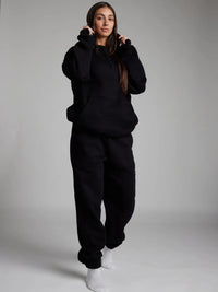 Person wearing a black hoodie and pants set on a plain background
