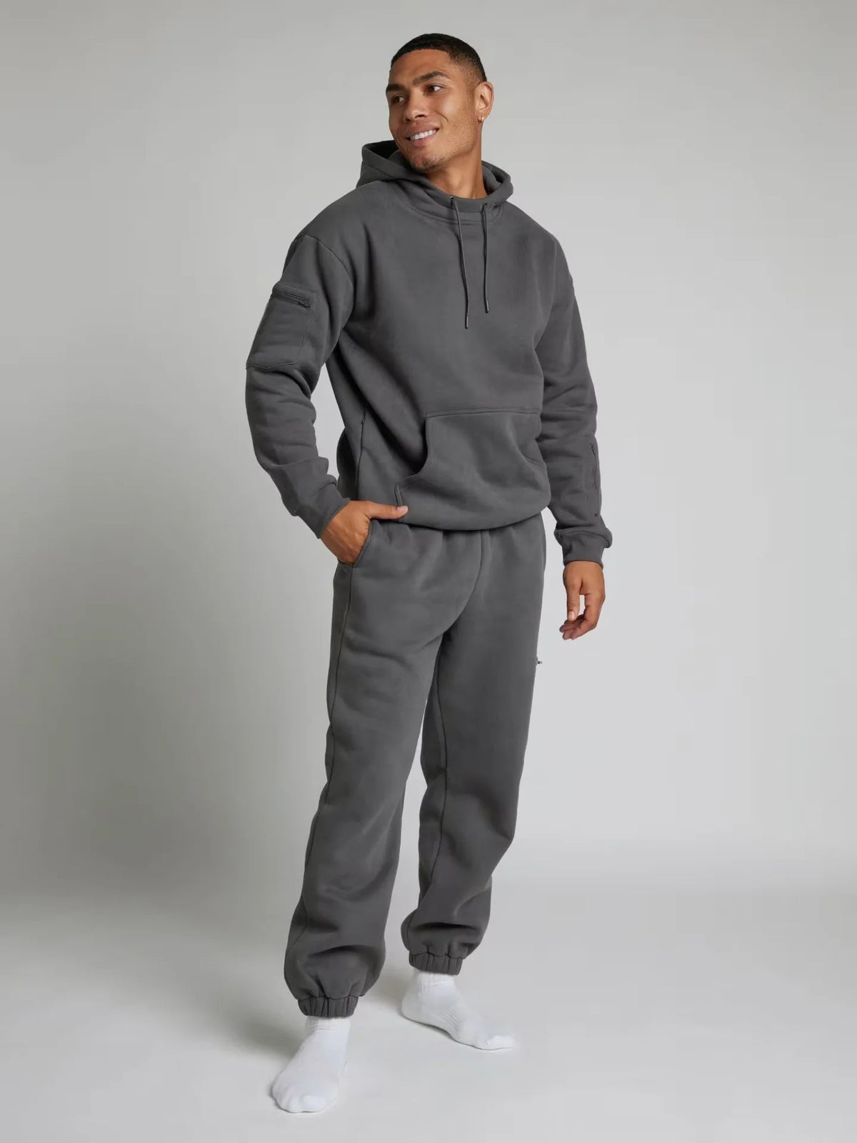 Man wearing a gray hoodie and sweatpants set on a plain background