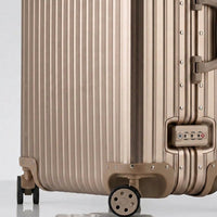 Close-up view of the integrated TSA-approved lock and silent multi-directional spinner wheels on The Masterpiece Legacy aluminum luggage by AERIA PRESTIGE in Aureum Gold.