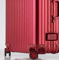 Close-up view of the integrated TSA-approved lock and silent multi-directional spinner wheels on The Masterpiece Legacy aluminum luggage by AERIA PRESTIGE in Imperial Red.