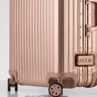 Close-up view of the integrated TSA-approved lock and silent multi-directional spinner wheels on The Masterpiece Legacy aluminum luggage by AERIA PRESTIGE in Rose Gold.