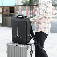 Person holding a black backpack on top of a silver suitcase outdoors.