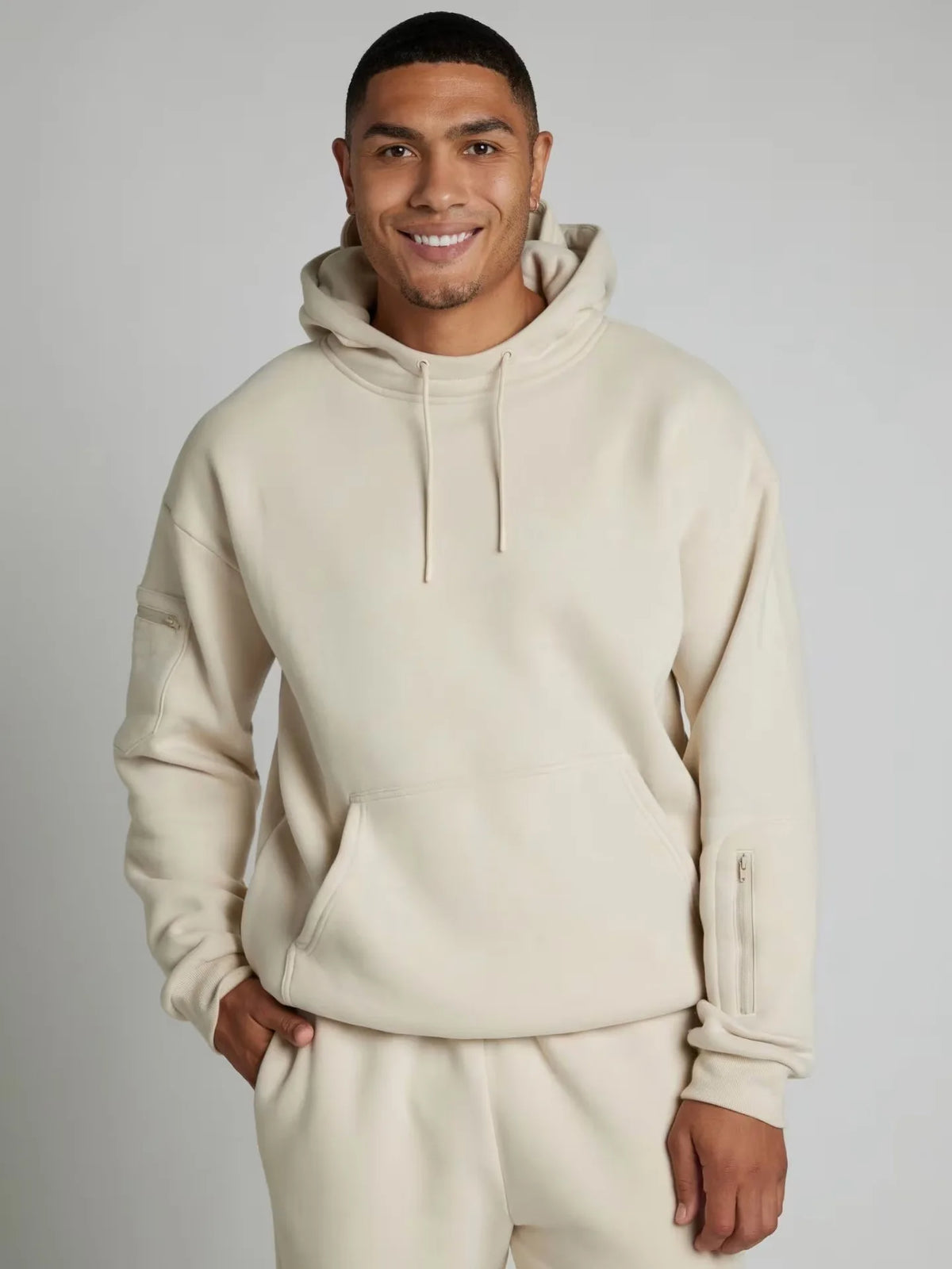 Man wearing a beige hoodie and pants on a plain background