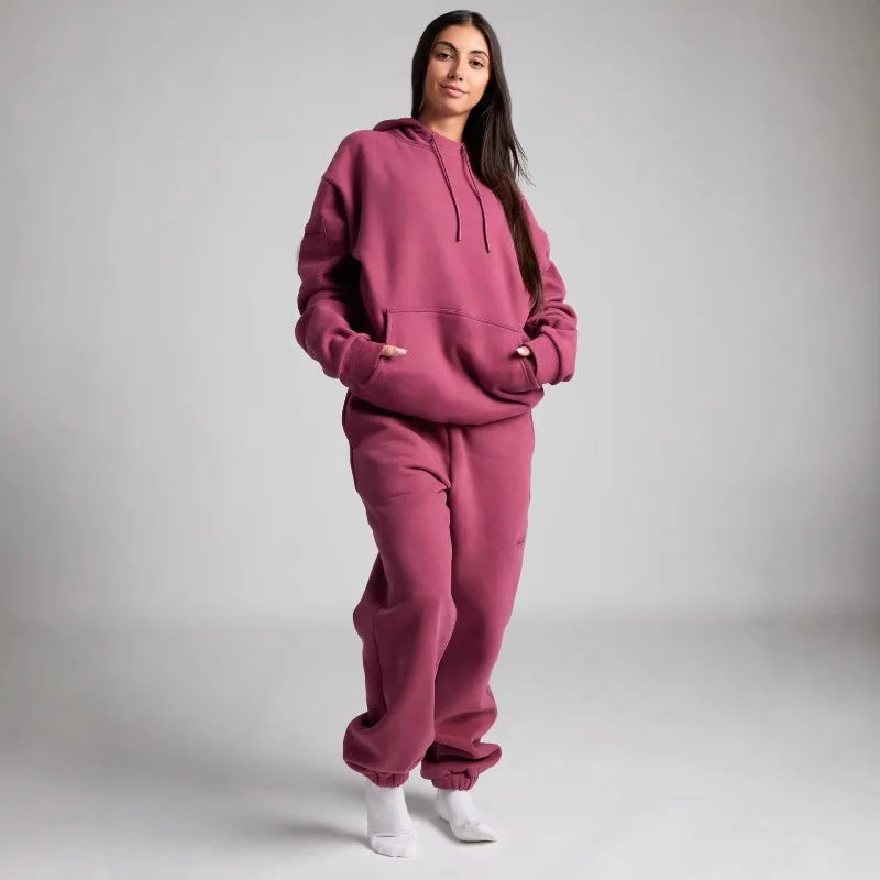 Person wearing a pink hoodie and pants set on a plain background