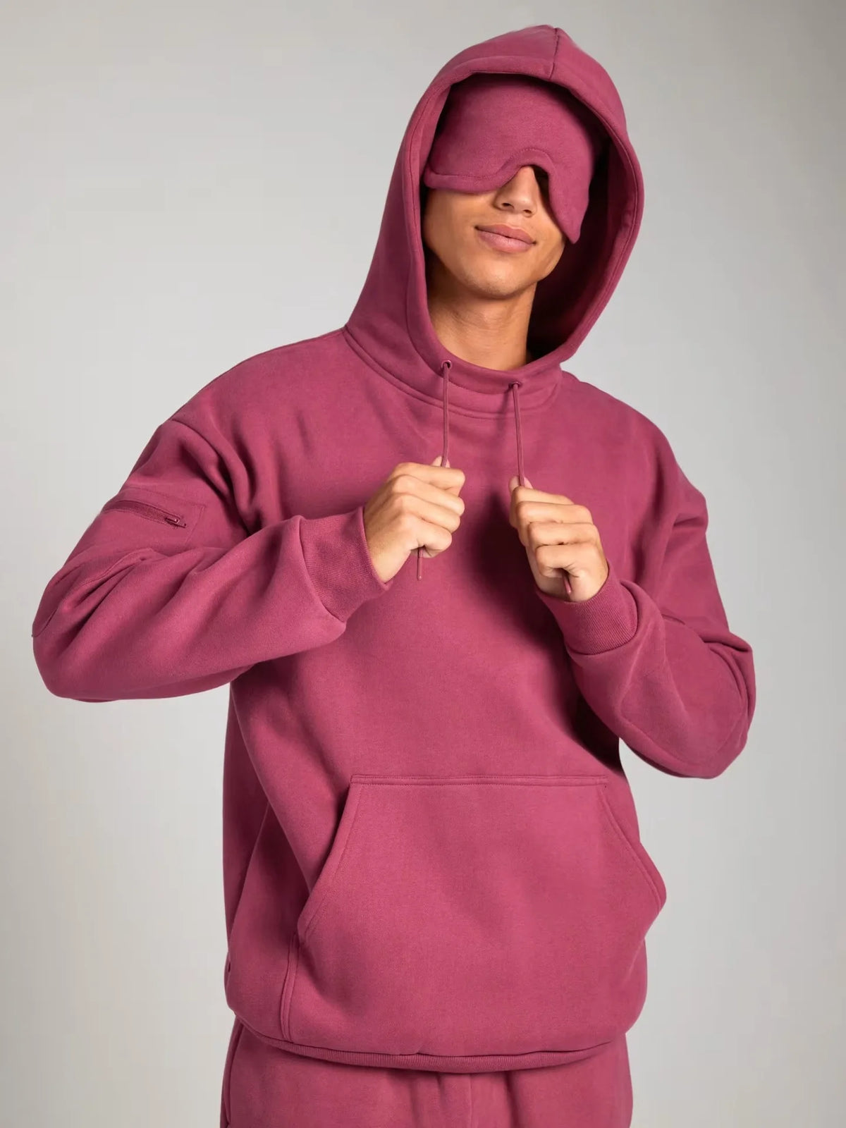 Person wearing a maroon hoodie with the hood over their eyes on a plain background