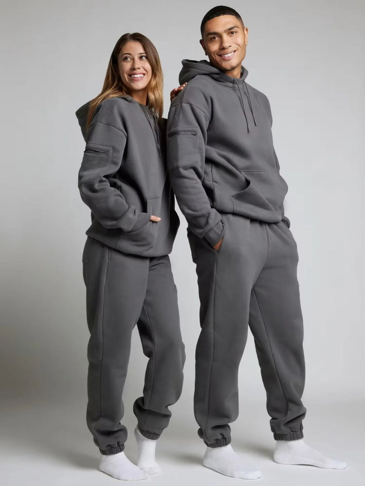 Two people wearing matching gray hoodie and sweatpants sets on a plain background