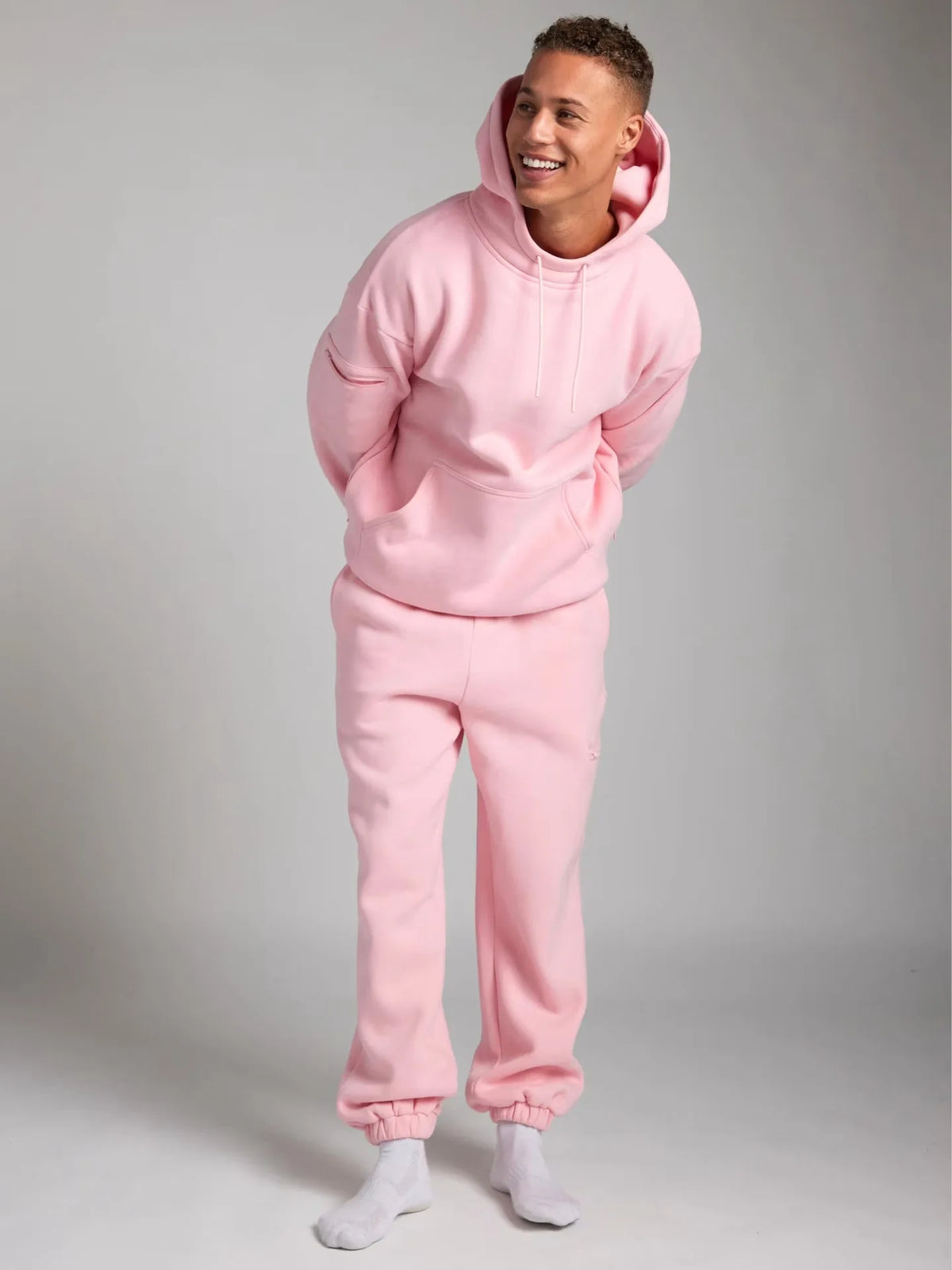 Person wearing a pink hoodie and pants set on a gray background