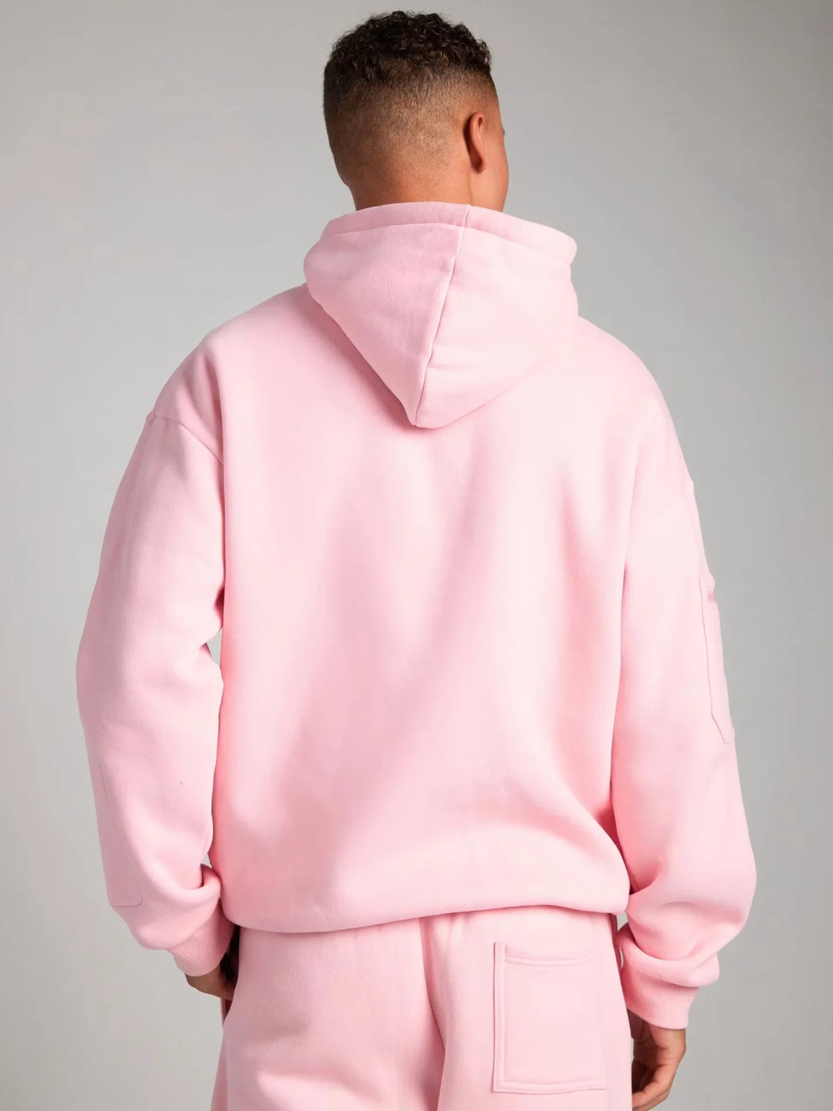 Person wearing a pink hoodie and pants against a gray background