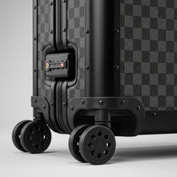 Detailed close-up of the Aeria Prestige The Monarch aluminum travel case, highlighting the Matte Obsidian Damier finish, robust corner riveting, smooth spinner wheels, and integrated TSA combination lock.