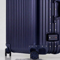 Close-up view of the integrated TSA-approved lock and silent multi-directional spinner wheels on The Masterpiece Legacy aluminum luggage by AERIA PRESTIGE in Abyssal Blue.