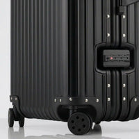 Close-up view of the integrated TSA-approved lock and silent multi-directional spinner wheels on The Masterpiece Legacy aluminum luggage by AERIA PRESTIGE in Matte Black.