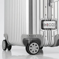 Close-up view of the integrated TSA-approved lock and silent multi-directional spinner wheels on The Masterpiece Legacy aluminum luggage by AERIA PRESTIGE in Sterling Silver.